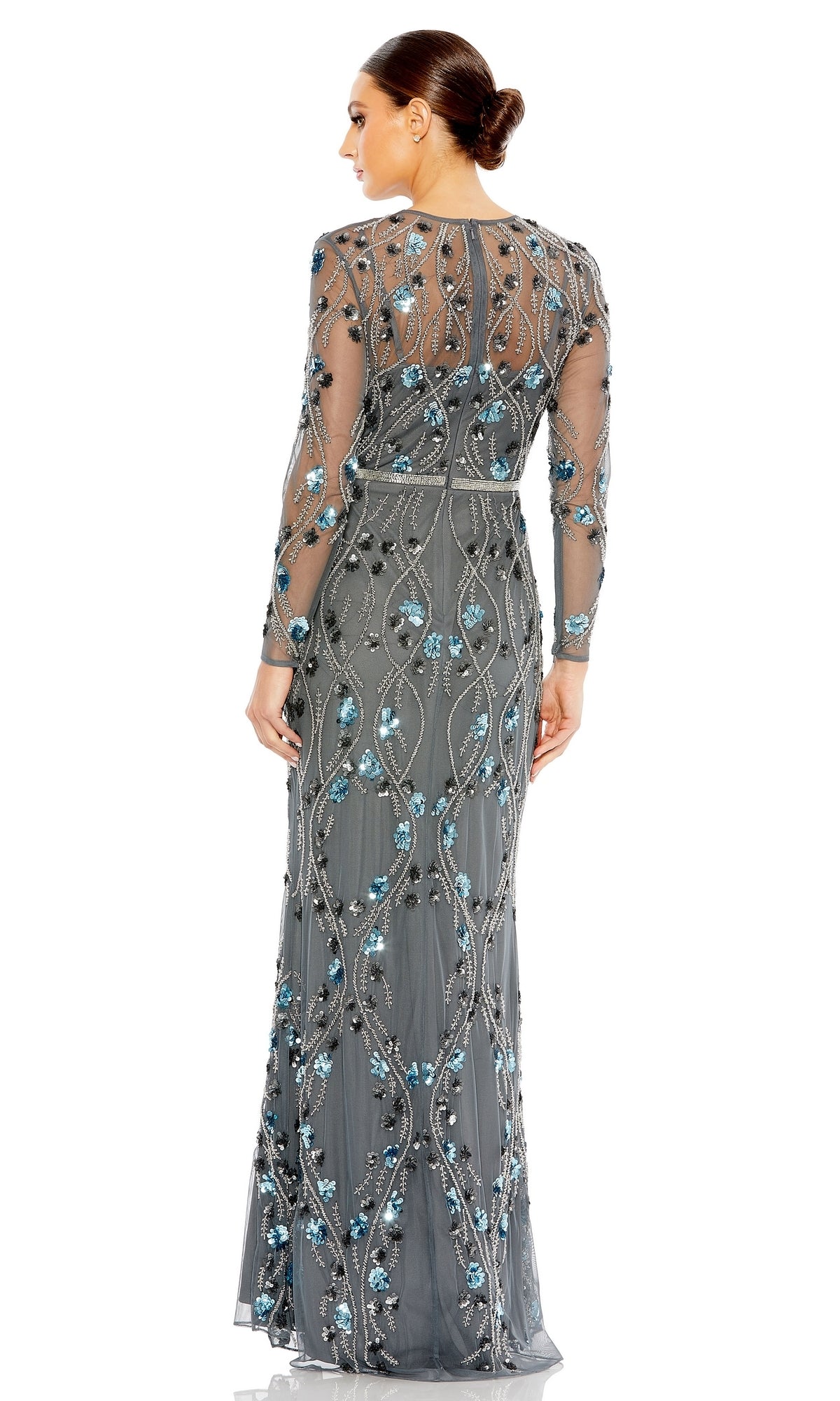 A woman faces away, wearing the Long Formal Dress 93772 by Mac Duggal—charcoal with long sleeves, sheer gray fabric, and blue and silver sequin embellishments. Her hair is in a low bun.